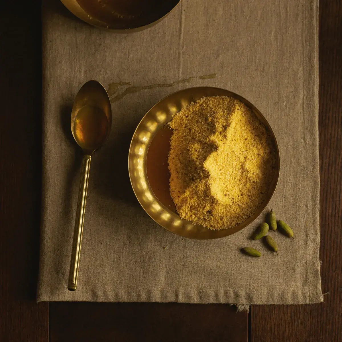 Besan in a brass bowl with ghee and cardamom on linen